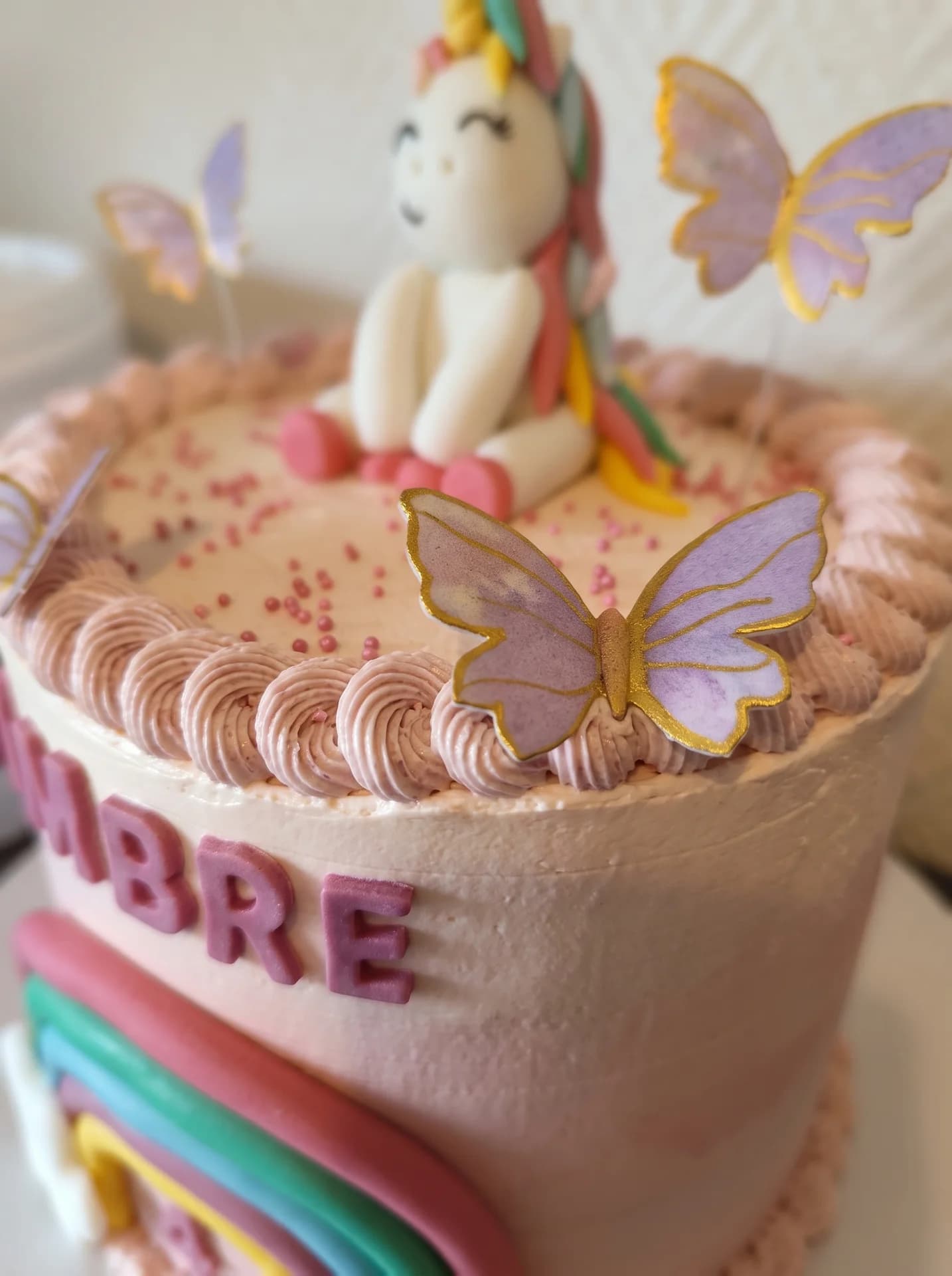Licorne blanche en pâte à sucre et papillons violets sur glaçage rose